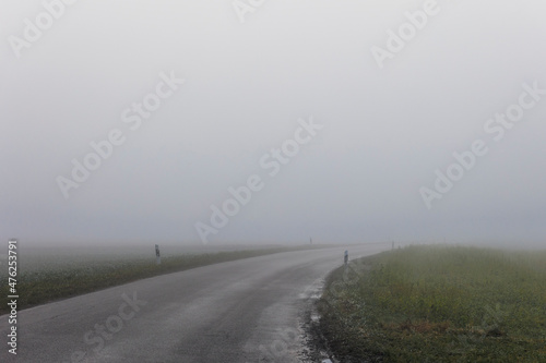 A country road in dense fog with the headlights of almost invisible vehicles