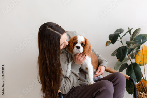 Fotografia Woman sitting in rattan chair with Cavalier King Charles Spaniel puppy
