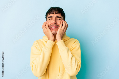 Young mixed race man isolated on blue background crying, unhappy with something, agony and confusion concept.