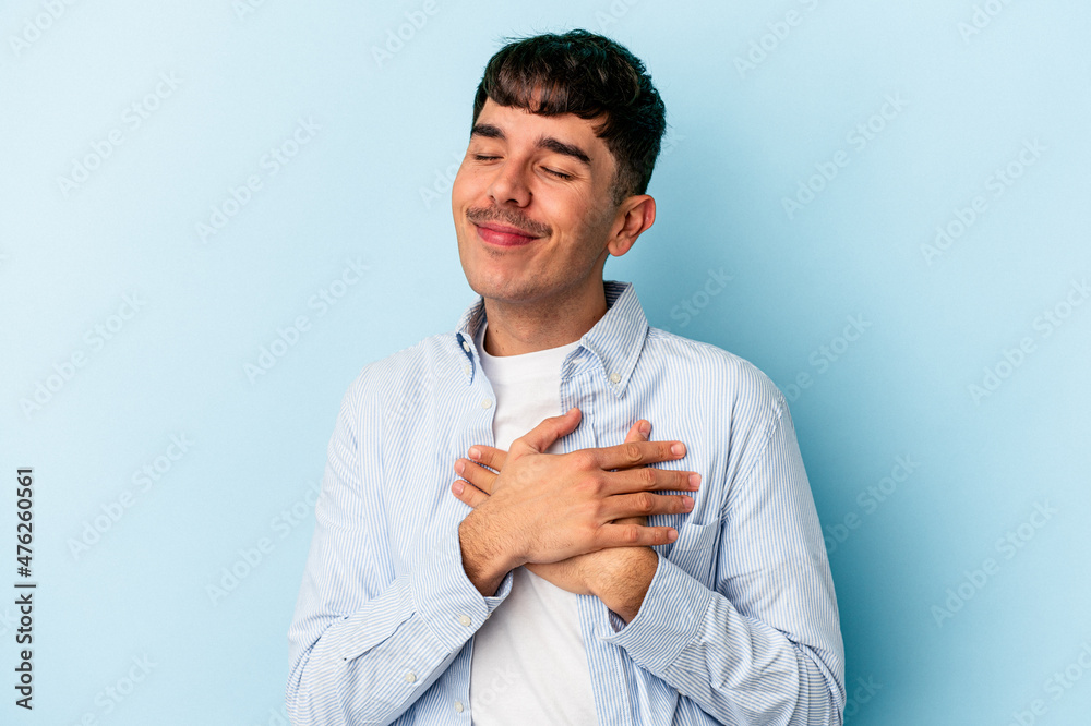 Young mixed race man isolated on blue background has friendly expression, pressing palm to chest. Love concept. Young mixed race man isolated on blue background has friendly expression, pressing palm to chest. Love concept.