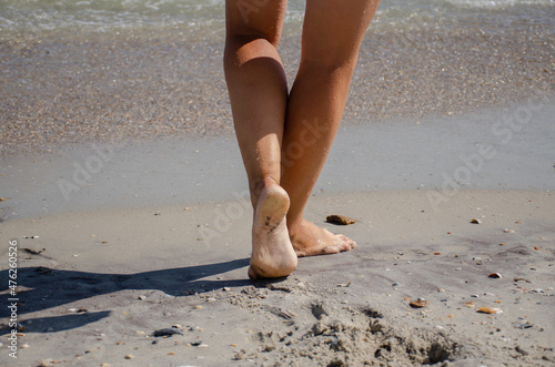 Women's feet walk on the sea sand on a sunny summer day. Relaxation and wellness concept