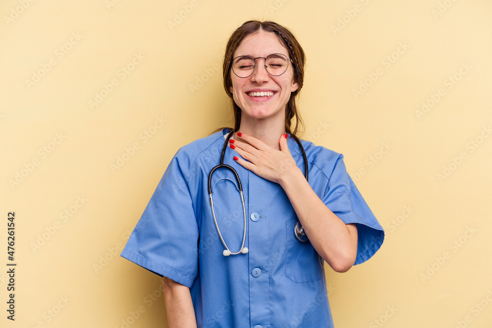 Young nurse caucasian woman isolated on yellow background laughs out loudly keeping hand on chest. Young nurse caucasian woman isolated on yellow background laughs out loudly keeping hand on chest.