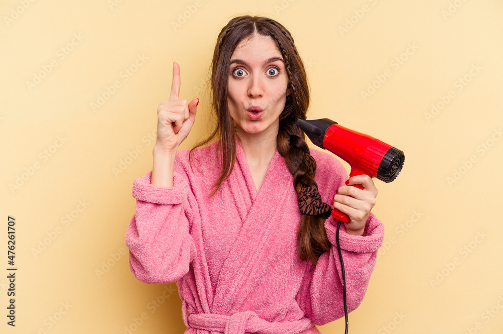 Young woman holding a hairdryer isolated on yellow background having some great idea, concept of creativity. Young woman holding a hairdryer isolated on yellow background having some great idea, concept of creativity.