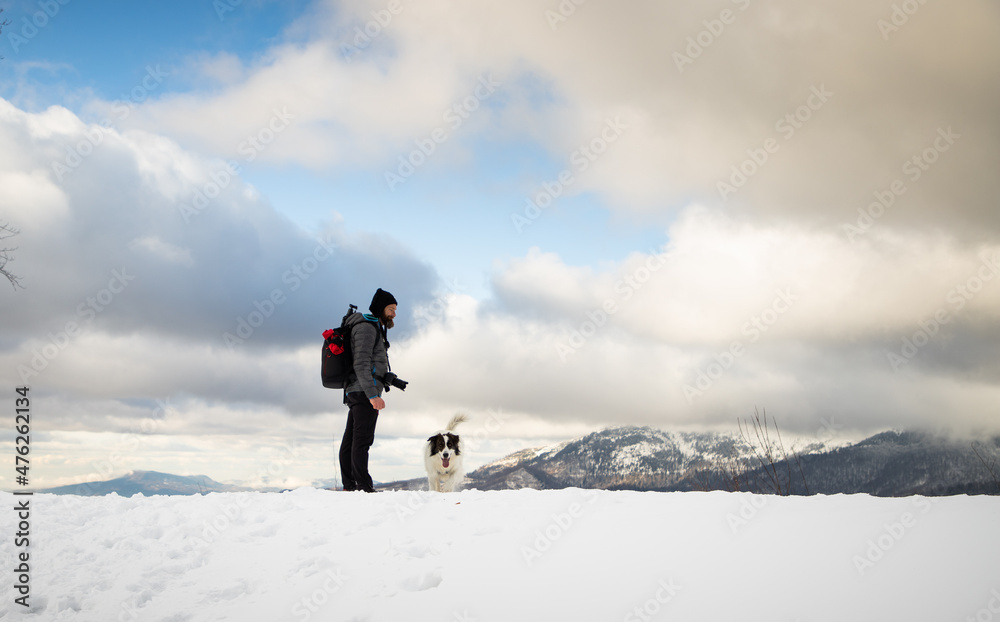 man and white dog trekking in winter mountains