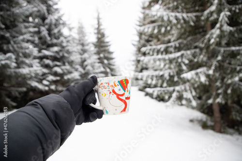 couple holding mugs with hot drinks in snowy winter landscape