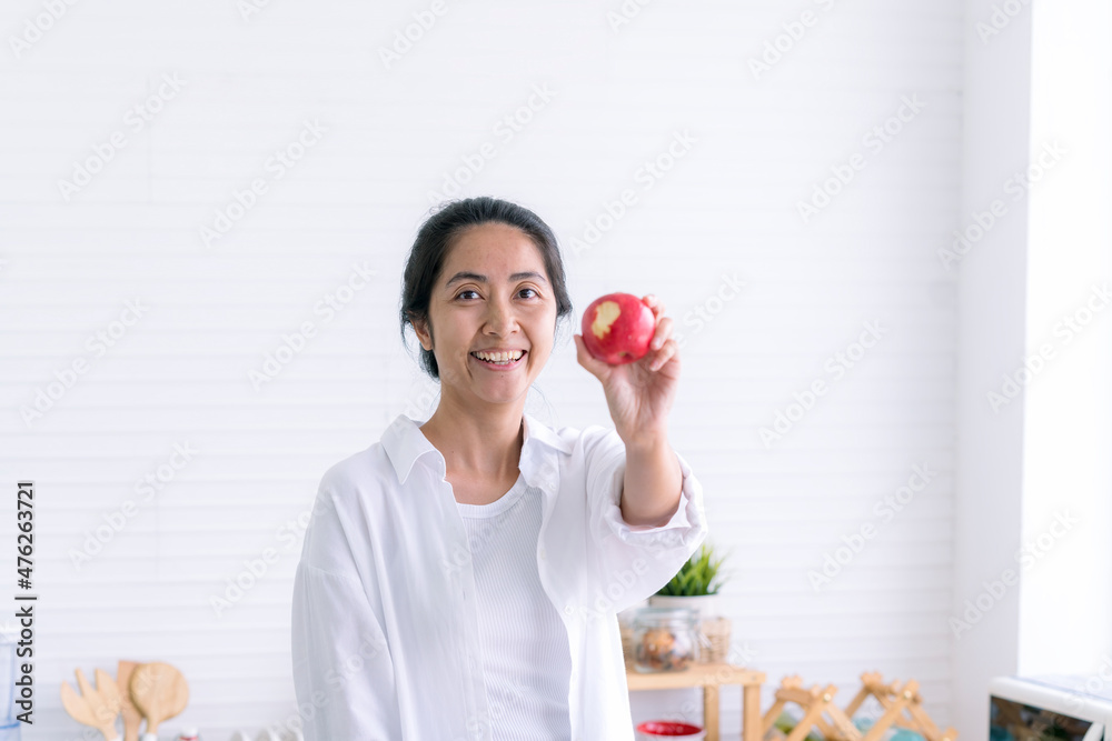 Asian woman showing bitten red apple in kitchen. Asian woman holding apples in the kitchen. Woman eating fresh apple while standing in the kitchen. Asian woman showing bitten red apple in kitchen. Asian woman holding apples in the kitchen. Woman eating fresh apple while standing in the kitchen.