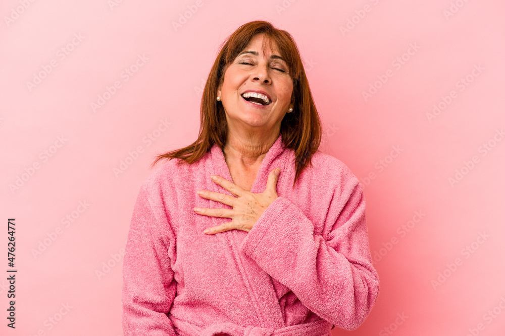 Middle age caucasian woman wearing a bathrobe isolated on pink background laughs out loudly keeping hand on chest.