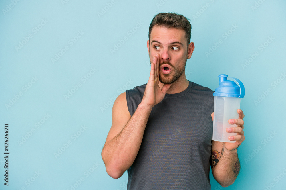 Young caucasian man drinking milkshake isolated on blue background is saying a secret hot braking news and looking aside Young caucasian man drinking milkshake isolated on blue background is saying a secret hot braking news and looking aside