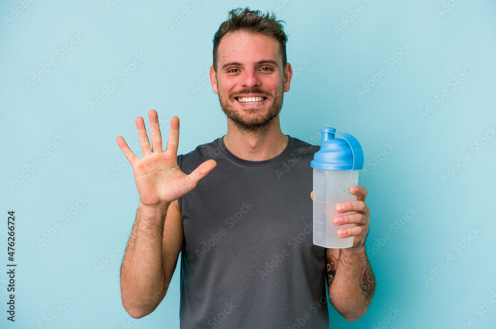 Young caucasian man drinking milkshake isolated on blue background smiling cheerful showing number five with fingers. Young caucasian man drinking milkshake isolated on blue background smiling cheerful showing number five with fingers.