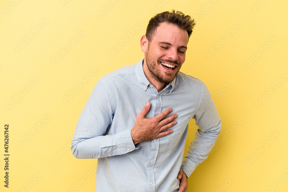 Young caucasian man isolated on yellow background laughing keeping hands on heart, concept of happiness. Young caucasian man isolated on yellow background laughing keeping hands on heart, concept of happiness.