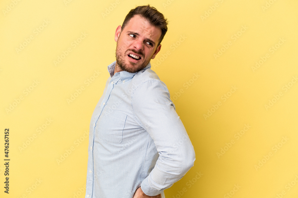 Young caucasian man isolated on yellow background suffering a back pain. Young caucasian man isolated on yellow background suffering a back pain.