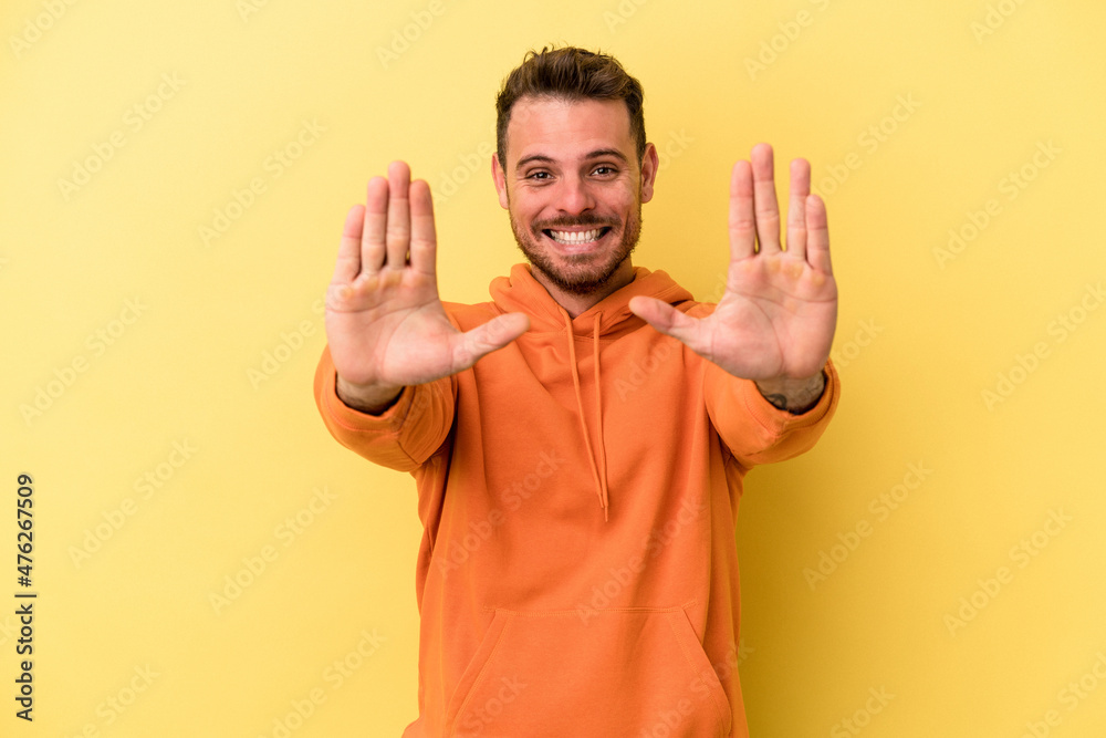 Young caucasian man isolated on yellow background showing number ten with hands. Young caucasian man isolated on yellow background showing number ten with hands.