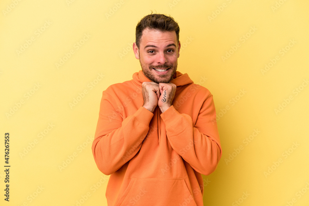 Young caucasian man isolated on yellow background keeps hands under chin, is looking happily aside. Young caucasian man isolated on yellow background keeps hands under chin, is looking happily aside.