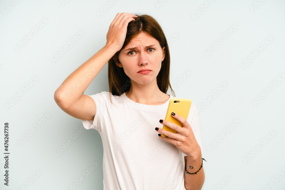 Young English woman holding mobile phone isolated on blue background being shocked, she has remembered important meeting. Young English woman holding mobile phone isolated on blue background being shocked, she has remembered important meeting.