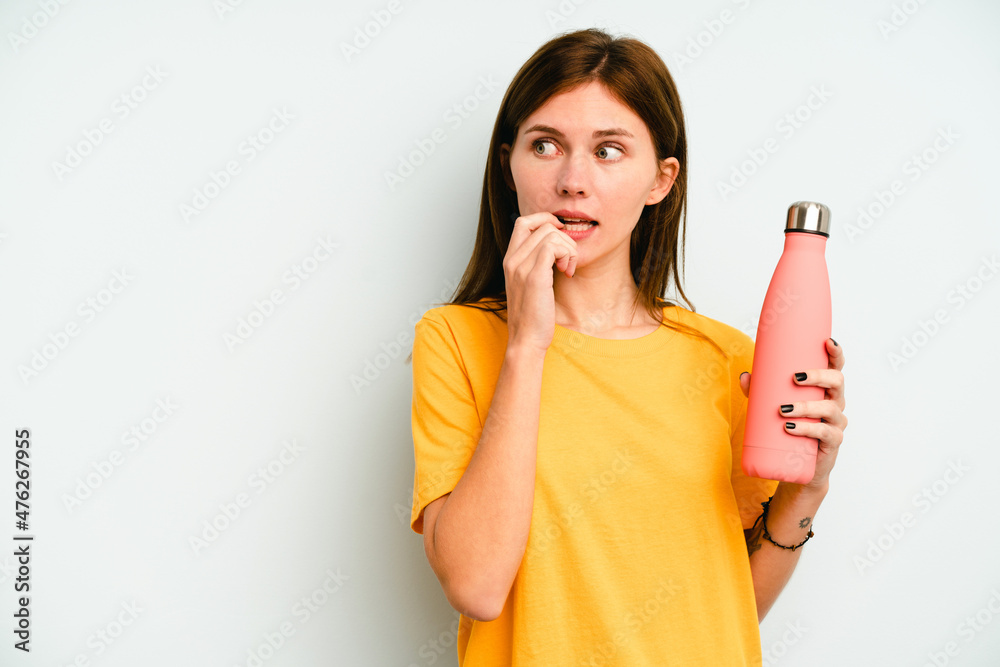 Young English woman holding a thermo isolated on blue background relaxed thinking about something looking at a copy space. Young English woman holding a thermo isolated on blue background relaxed thinking about something looking at a copy space.