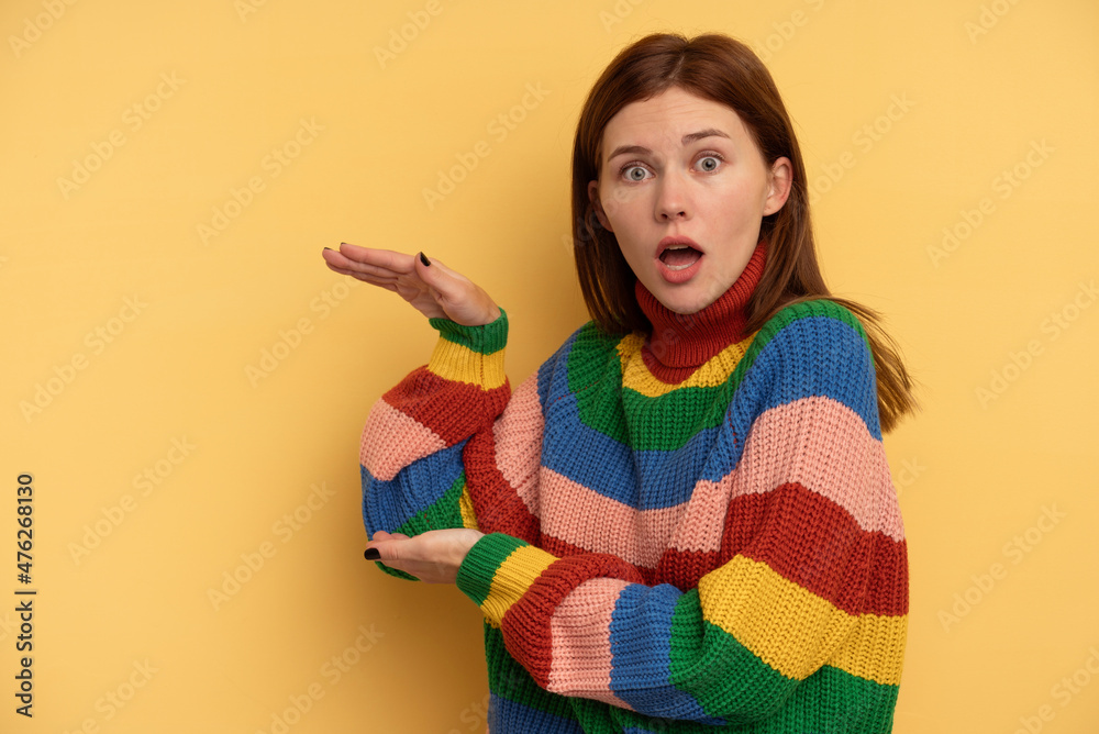 Young English woman isolated on yellow background shocked and amazed holding a copy space between hands. Young English woman isolated on yellow background shocked and amazed holding a copy space between hands.