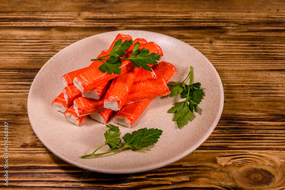 Ceramic plate with pile of crab sticks and parsley twig on a wooden table Ceramic plate with pile of crab sticks and parsley twig on a wooden table