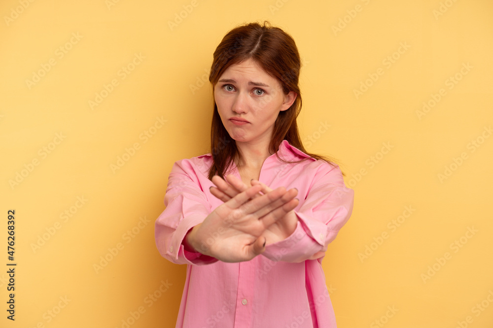 Young English woman isolated on yellow background standing with outstretched hand showing stop sign, preventing you. Young English woman isolated on yellow background standing with outstretched hand showing stop sign, preventing you.