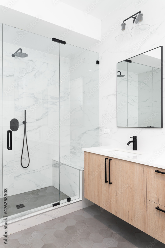 A beautiful luxury, modern bathroom with a light wood cabinet, walk-in shower with marble tiled walls, and black faucets and hardware. - obrazy, fototapety, plakaty 