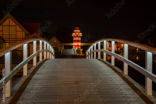 Nächtlicher Weg über eine weiße Rundbrücke zu einem beleuchteten rot-weißen Leuchtturm