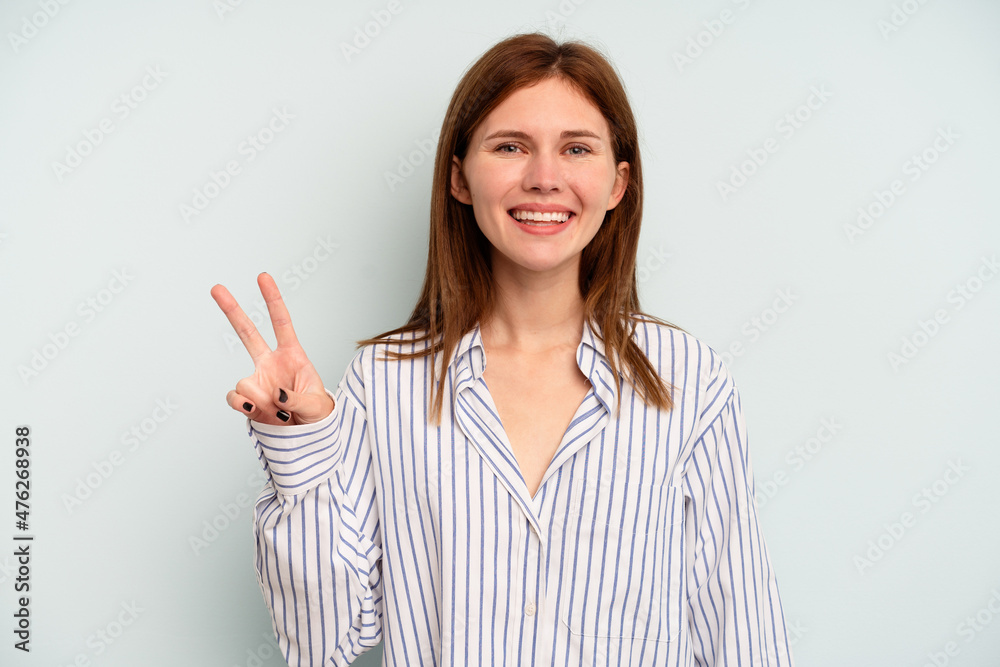 Young English woman isolated on blue background showing victory sign and smiling broadly. Young English woman isolated on blue background showing victory sign and smiling broadly.