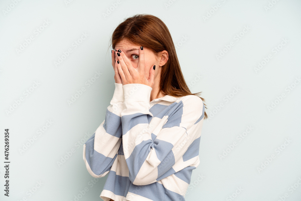 Young English woman isolated on blue background blink through fingers frightened and nervous. Young English woman isolated on blue background blink through fingers frightened and nervous.
