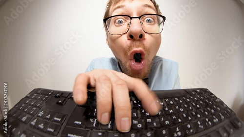 Fisheye portrait of crazy nerd with glasses typing keyboard, looking at camera