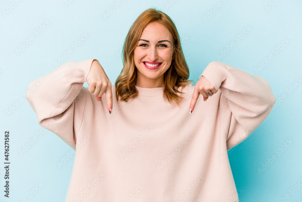 Young caucasian woman isolated on blue background points down with fingers, positive feeling. Young caucasian woman isolated on blue background points down with fingers, positive feeling.