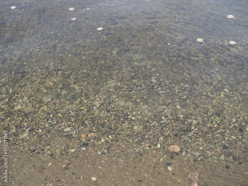 The texture of the bottom. Many small stones are visible under the clear water. Water ripples of the sea, sun rays on the rocks