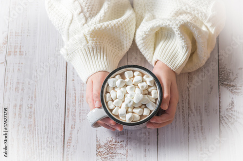 Person holds a mug of hot chocolate with marshmallows on top on a wooden background