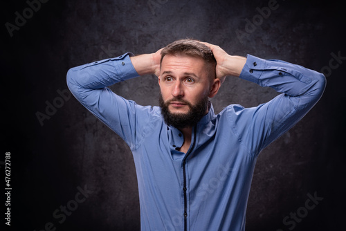 Young bearded European guy imitates surprise and excitement with radical emotions holding his head with his hands. For advertising