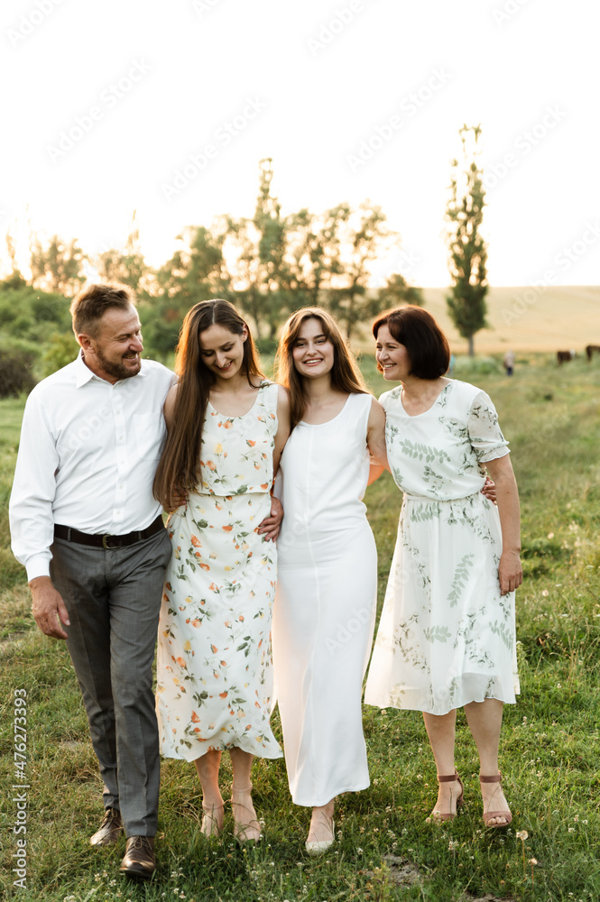 father and mother of middle age tenderly hug two adult daughters in nature. beautiful family walks across the field at sunset of the day. parents with older children father and mother of middle age tenderly hug two adult daughters in nature. beautiful family walks across the field at sunset of the day. parents with older children