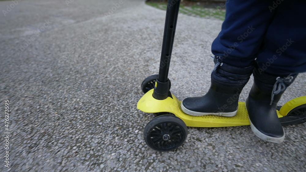 Obraz premium Child legs riding toy scooter outside wearing boots