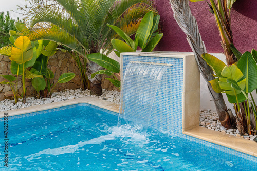 Close-up of a fountain waterfall in a luxury pool near the hotel with palm trees for tourists.