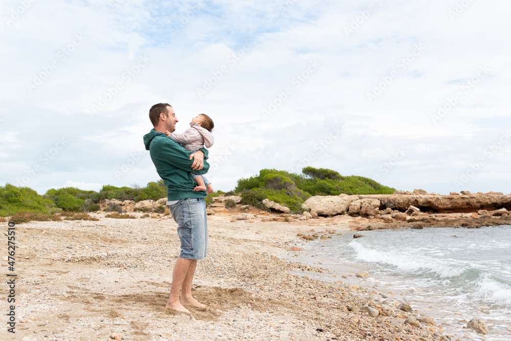 Young man holding his little girl and laughing together at the beach. Travel and happiness at the mediterranean coast.