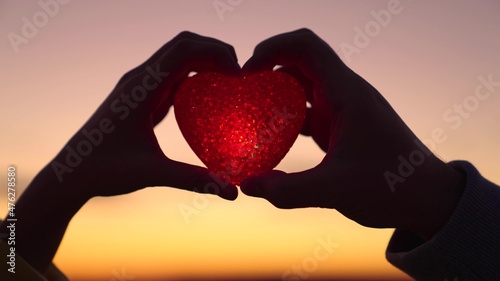 Health  take care of your heart  cardiology medicine. Young girl holds beautiful red heart in her hands against sunset background. Woman in love with red flashlight heart symbol. valentines day.