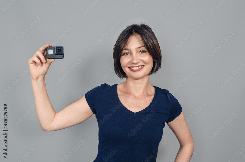 Porter of woman with short black hair holding a camera with one hand. Smiling looking at camera. Gopro. Action camera. Porter of woman with short black hair holding a camera with one hand. Smiling looking at camera. Gopro. Action camera.