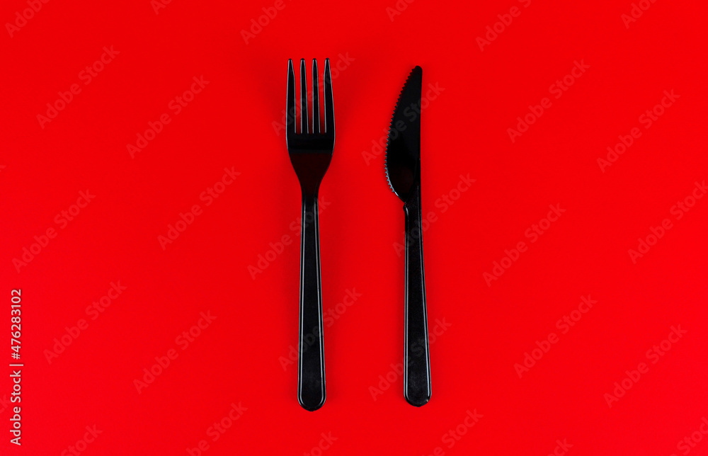 Black plastic fork and knife against red background Black plastic fork and knife against red background