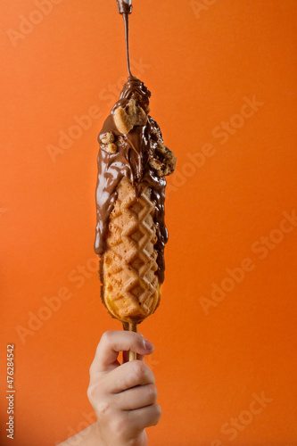 waffle stick glazed with chocolate an cookies. a child hand is holding it. orange background