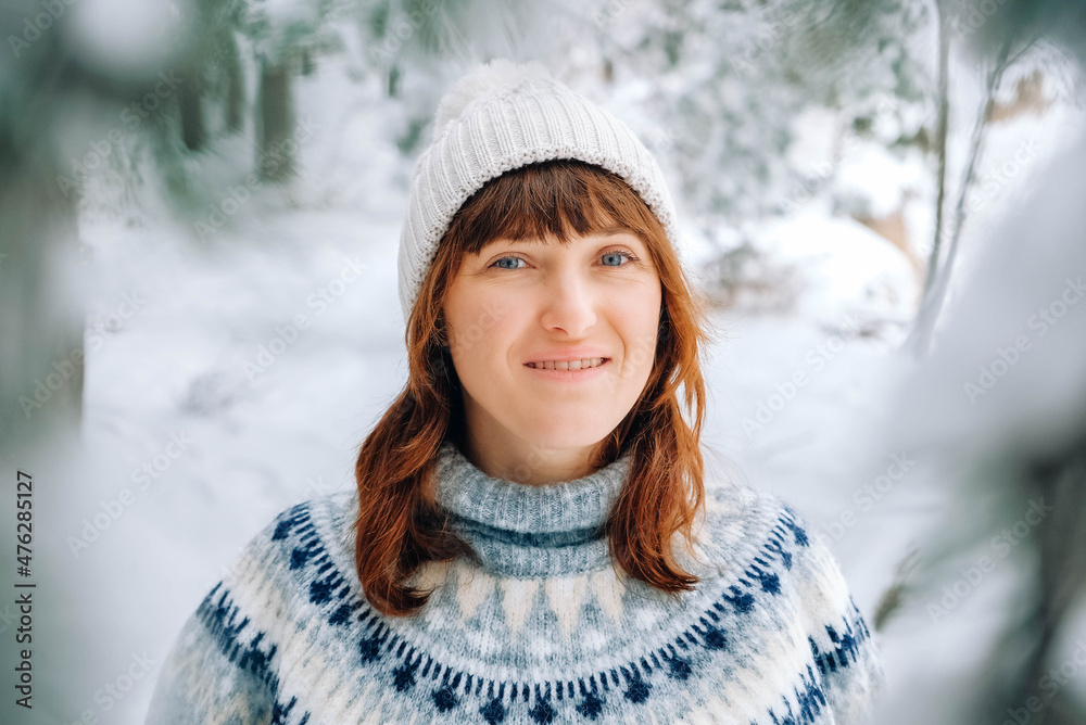 Winter portrait of a woman in a warm hat and sweater on a background of snowy forest Winter portrait of a woman in a warm hat and sweater on a background of snowy forest
