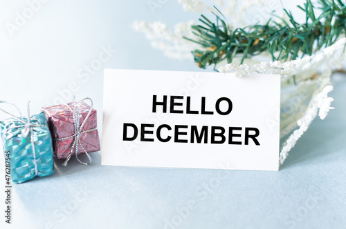 Hello December inscription on the card next to two gifts in a package on a light background