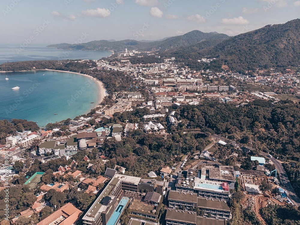 Aerial image with kata beach. Resort town with buildings and different areas and bunch of trees around. Background of impressive mountains. On the side there is blue and azure sea and sandy coast.