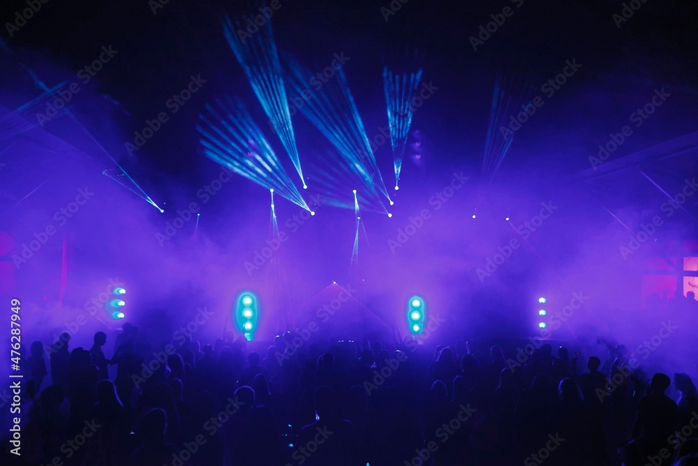Happy people are dancing and having fun at holiday party in nightclub. Crowd of guys celebrate concert event. Entire club is illuminated by blue and purple floodlights and lanterns. Youth fun concept.