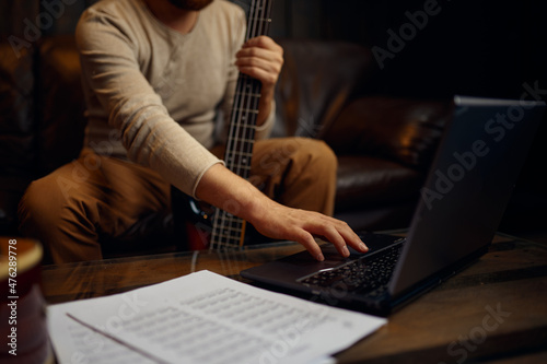 Young man learning playing guitar through internet