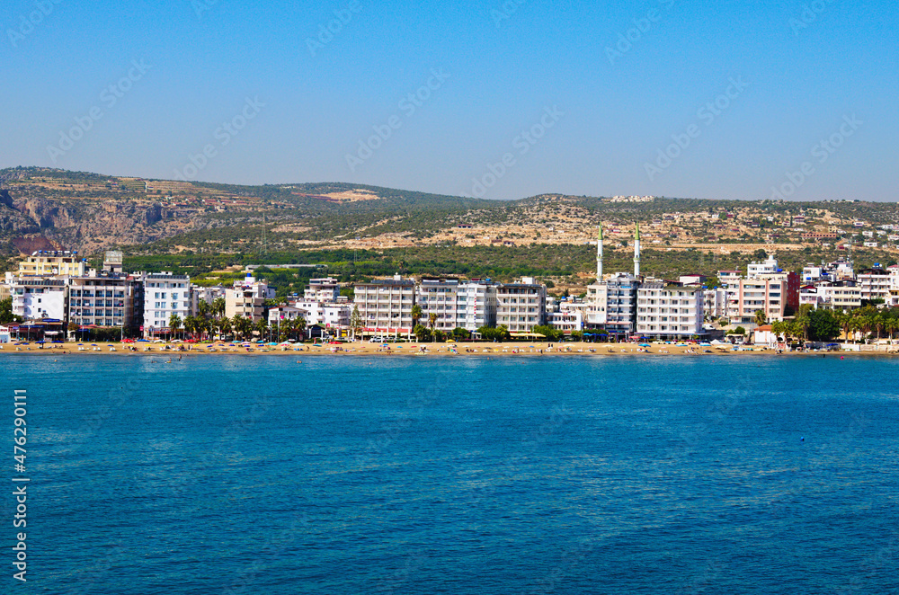 Kizkalesi, Turkey-October 11,2021: Wide angle landscape view of blue water of Mediterranean Sea and city beach, embankment with many hotels in Kizkalesi. Blue sky background. Famous touristic place