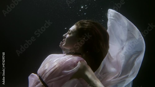 romantic ballerina is floating gracefully underwater, medium portrait in dark water