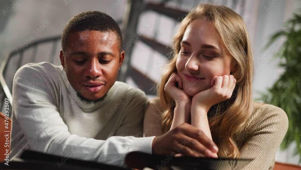 African-American guy and happy white woman friend enjoy family memories looking at old yellowed pictures in photo-book at home closeup slow motion African-American guy and happy white woman friend enjoy family memories looking at old yellowed pictures in photo-book at home closeup slow motion