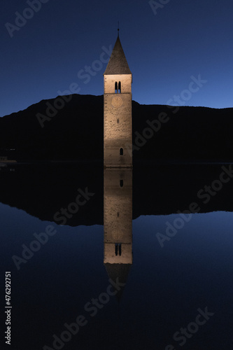 Vertical shot of the stone tower in Reschen Pass, Italy reflecting in the water next to it photo