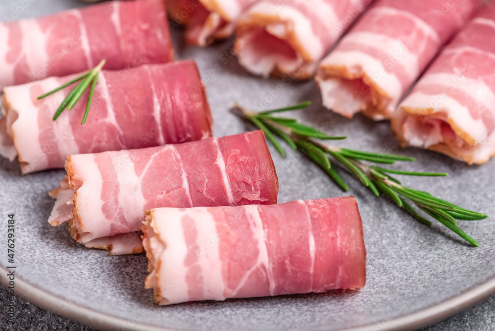 Raw smoked bacon roll with rosemary close-up. Selective focus. Side view Raw smoked bacon roll with rosemary close-up. Selective focus. Side view