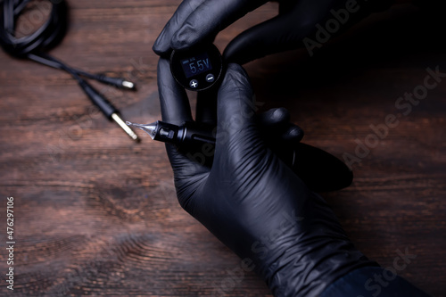 the hands of the permanent makeup artist in black sterile gloves are trying to set the voltage on the wireless block from the tattoo machine